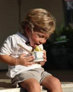 A young boy enthusiastically enjoys a Greek frozen yogurt from Mythos, with a spoon in hand.