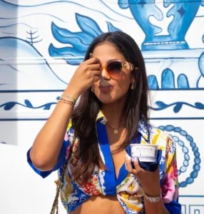 A woman holds a Mythos bottle against a blue and white patterned wall in Italy.