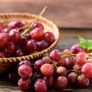 A basket of fresh, ripe red grapes sits on a wooden surface.