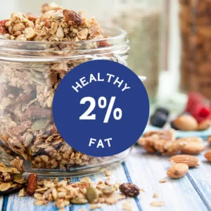 A jar of healthy granola with nuts and seeds sits on a wooden table with blueberries and almonds.